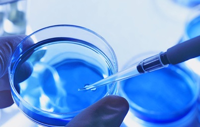 Pipette extracting liquid from a petri dish, bathed in blue hues