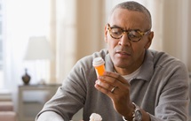 Photograph of man with studious but concerned expression studying a medication bottle
