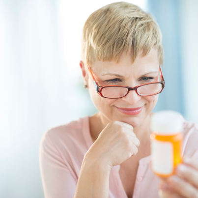 Woman wearing glasses low on her nose looking at a medication bottle, and smiling slightly