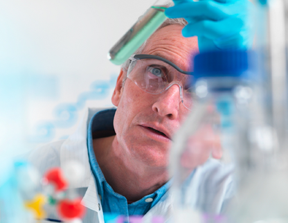 A researcher wearing a white lab coat carefully and attentively examining a test tube of green liquid