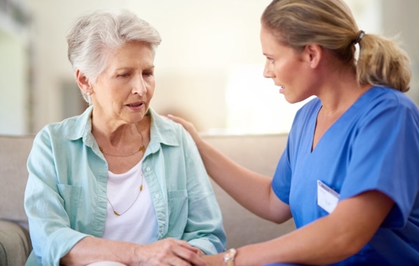 Older female patient with a worried expression being comforted by a healthcare professional