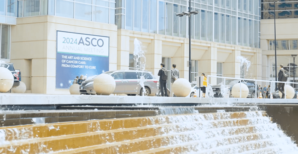 The front of a conference center with a fountain and people milling about in the foreground, with the ASCO 2024 Annual Meeting sign on the front of the conference center