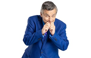 Man in a blue suit snickering, hiding his mouth behind his hands