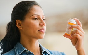 A photograph of a woman reading the label on a medication bottle she is holding high, directly in front of her eyes