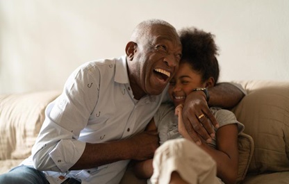 An African American grandfather hugging his granddaughter, both laughing