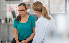 Woman with expression of nervous concern is comforted by her doctor