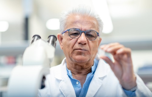 Selective focus shot of a male chemist as he holds a slide containing a medical sample with a serious expression on their face.