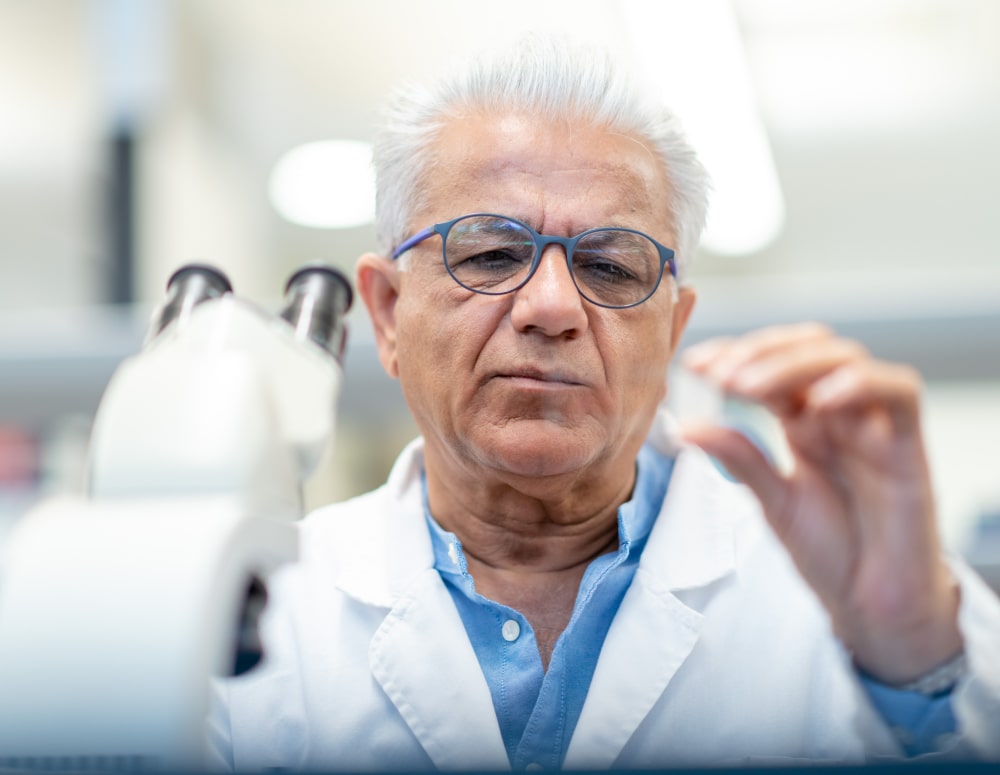 Selective focus shot of a male chemist as he holds a slide containing a medical sample with a serious expression on their face.